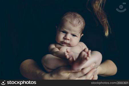 Nude baby girl posing in her mother&rsquo;s arms on black background. Nude baby posing in her mother&rsquo;s arms