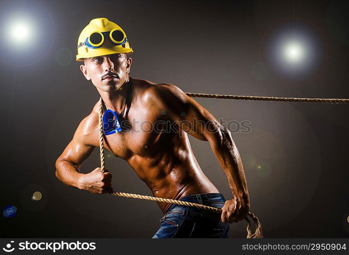 Nude builder pulling rope in darkness