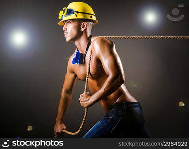 Nude builder pulling rope in darkness