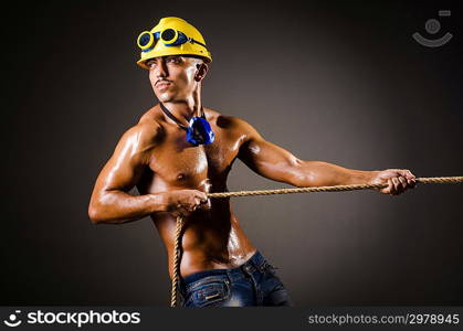 Nude builder pulling rope in darkness