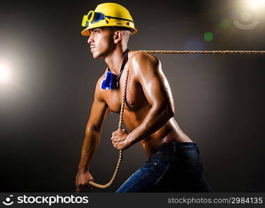 Nude builder pulling rope in darkness