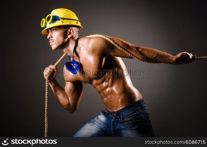 Nude builder pulling rope in darkness