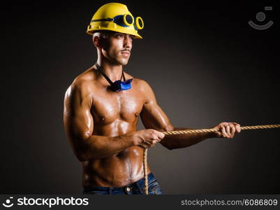 Nude builder pulling rope in darkness