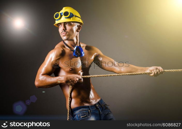 Nude builder pulling rope in darkness