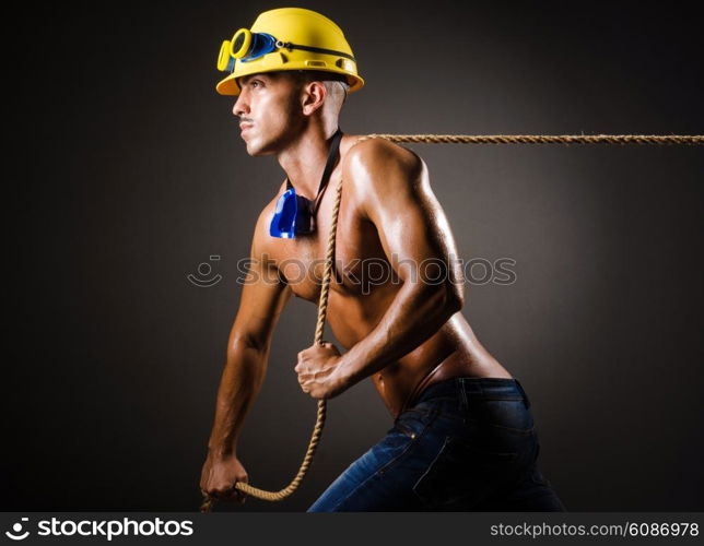 Nude builder pulling rope in darkness