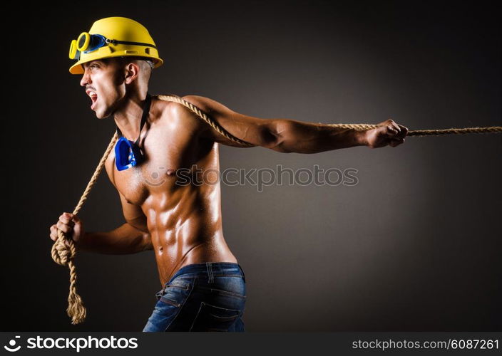 Nude builder pulling rope in darkness