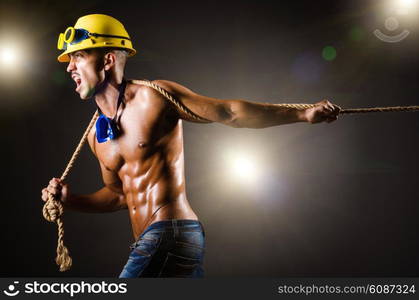 Nude builder pulling rope in darkness