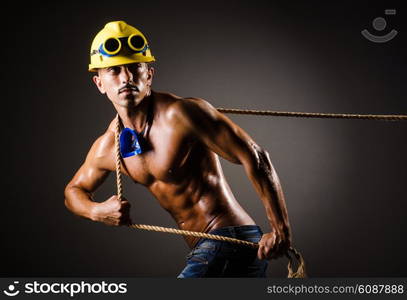 Nude builder pulling rope in darkness