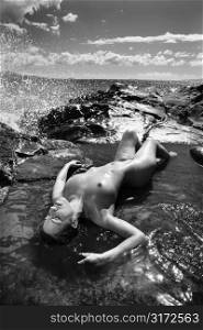 Nude Caucasian mid adult woman lying on back in tidal pool at Maui coast with eyes closed.