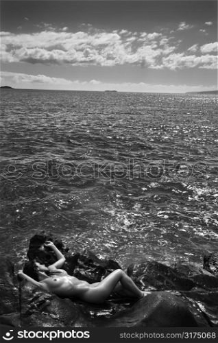Nude Caucasian mid adult woman nestled in watery alcove at Maui coast.