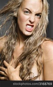 Nude Caucasian woman pulling long blond hair and looking at viewer with snarling expression.