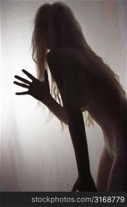 Nude Caucasian woman silhouetted behind sheer cloth waving.