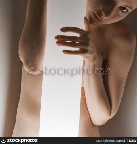 Nude Caucasian woman standing behind light pole looking at viewer.