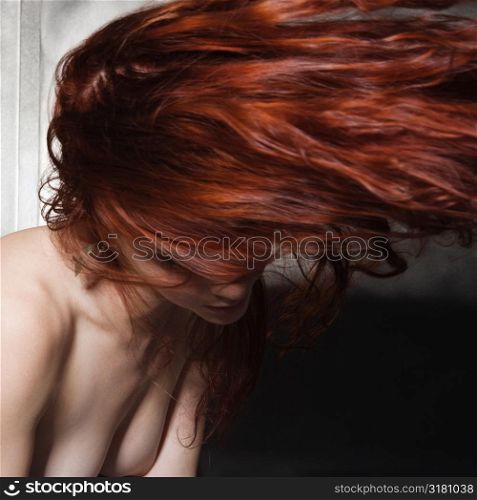 Nude Caucasian woman with long hair blowing in air.