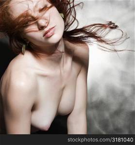 Nude Caucasian woman with long hair blowing in air.
