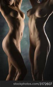 Nude Hispanic and Caucasian women standing facing each other with arms raised over head.