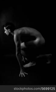 Nude male athlete preparing for the start on black background