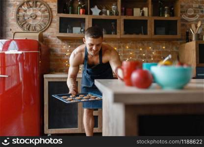 Nude man in apron cooking pastry on the kitchen. Naked male person preparing breakfast at home, food preparation without clothes