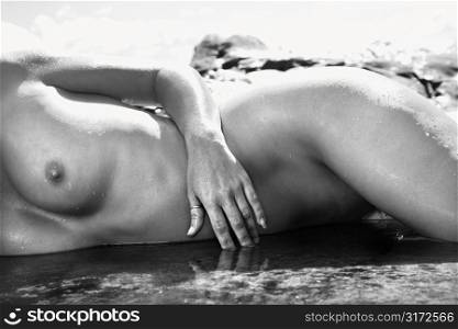 Nude midsection of Caucasian mid adult woman lying on side in water at Maui coast.
