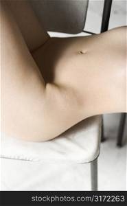 Nude womans torso sitting on chair.