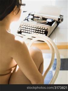 Nude young Asian woman sitting at typewriter,