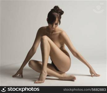 Nude, young, natural, sensual woman with brown hair and hair bun posing in studio