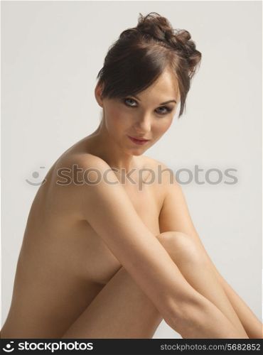 Nude, young, natural skin, sensual woman sitting on white and looking in camera smiling