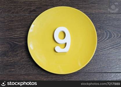 Number nine on the yellow plate and brown background.. Number nine on the yellow plate.