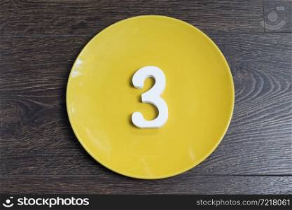 Number three on the yellow plate and brown background.. Number three on the yellow plate.