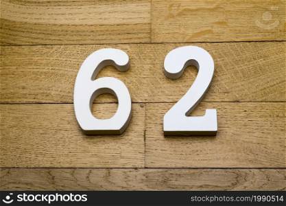 Numbers sixty-two on the wooden parquet floor in the background.. Figures sixty two on a wooden, parquet floor.