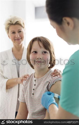 Nurse applying bandage on boy arm with mother at hospital