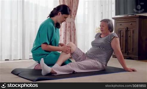 Nurse giving leg massage to senior woman in a retirement home. Physiotherapist nurse helping an elderly women physical rehabilitation at home. Slow motion hand held movement