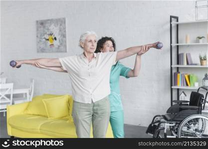 nurse helping her senior female patient exercising with dumbbells