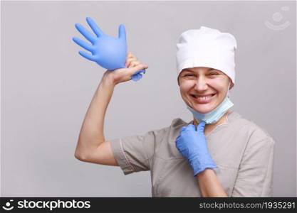 Nurse or doctor holding or putting on blue gloves isolated on white background. funny smiling female nurse or doctor in medical uniform and protective mask holding inflated blue latex glove isolated on white background