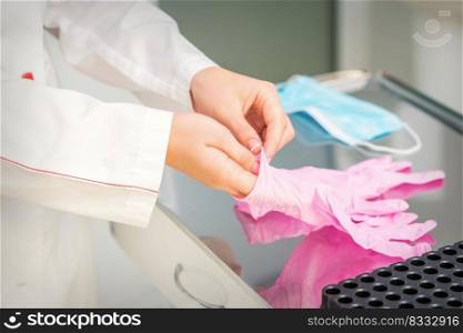 Nurse’s hands putting on pink sterilized protective gloves in the laboratory. Nurse’s hands putting on pink gloves