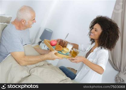 nurse serving breakfast to senior man in bedroom