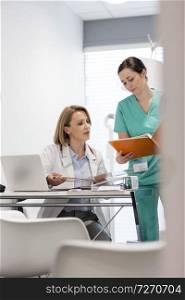 Nurse showing medical file to mature doctor at desk in hospital