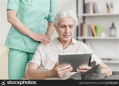 nurse standing near senior woman using digital tablet