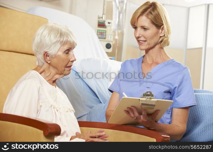 Nurse Taking Notes From Senior Female Patient Seated In Chair By Hospital Bed