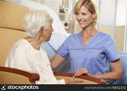 Nurse Taking To Senior Female Patient Seated In Chair By Hospital Bed