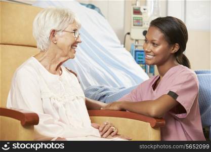 Nurse Talking To Senior Female Patient Seated In Chair By Hospital Bed