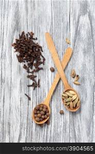 Nutmeg, clove and allspice in old spoon on wooden background