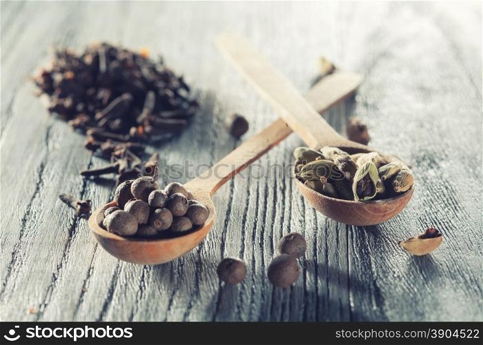 Nutmeg, clove and allspice in old spoon on wooden background. Photo with cross processing filter