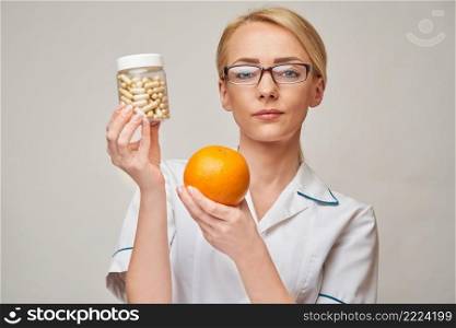 nutritionist doctor healthy lifestyle concept - holding orange fruit and nutrition vitamin capsules or pills.. nutritionist doctor healthy lifestyle concept - holding orange fruit and nutrition vitamin capsules or pills