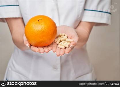 nutritionist doctor healthy lifestyle concept - holding orange fruit and nutrition vitamin capsules or pills.. nutritionist doctor healthy lifestyle concept - holding orange fruit and nutrition vitamin capsules or pills