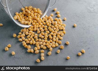 Nutritious dry chickpeas spilled from sieve on grey background. High energy food. Healthy snack. Protein organic product