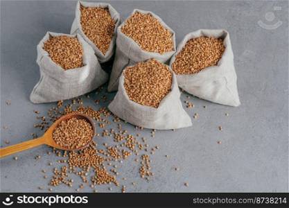 Nutritious ingredient containing vitamins. Shot of linen sacks with buckwheat against grey background. Organic food. Healthy nutrition