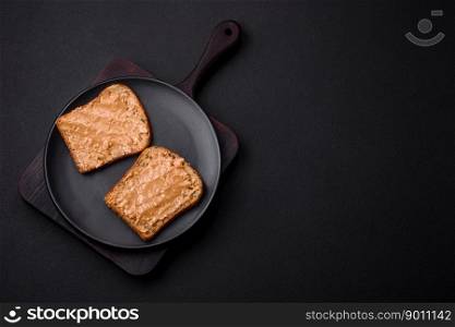 Nutritious sandwich consisting of bread and peanut butter on a black ceramic plate on a dark concrete background
