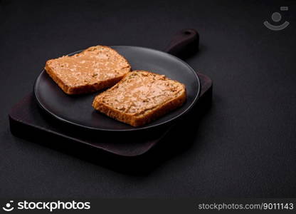 Nutritious sandwich consisting of bread and peanut butter on a black ceramic plate on a dark concrete background