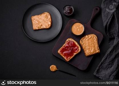 Nutritious sandwiches consisting of bread, raspberry jam and peanut butter on a black ceramic plate on a dark concrete background